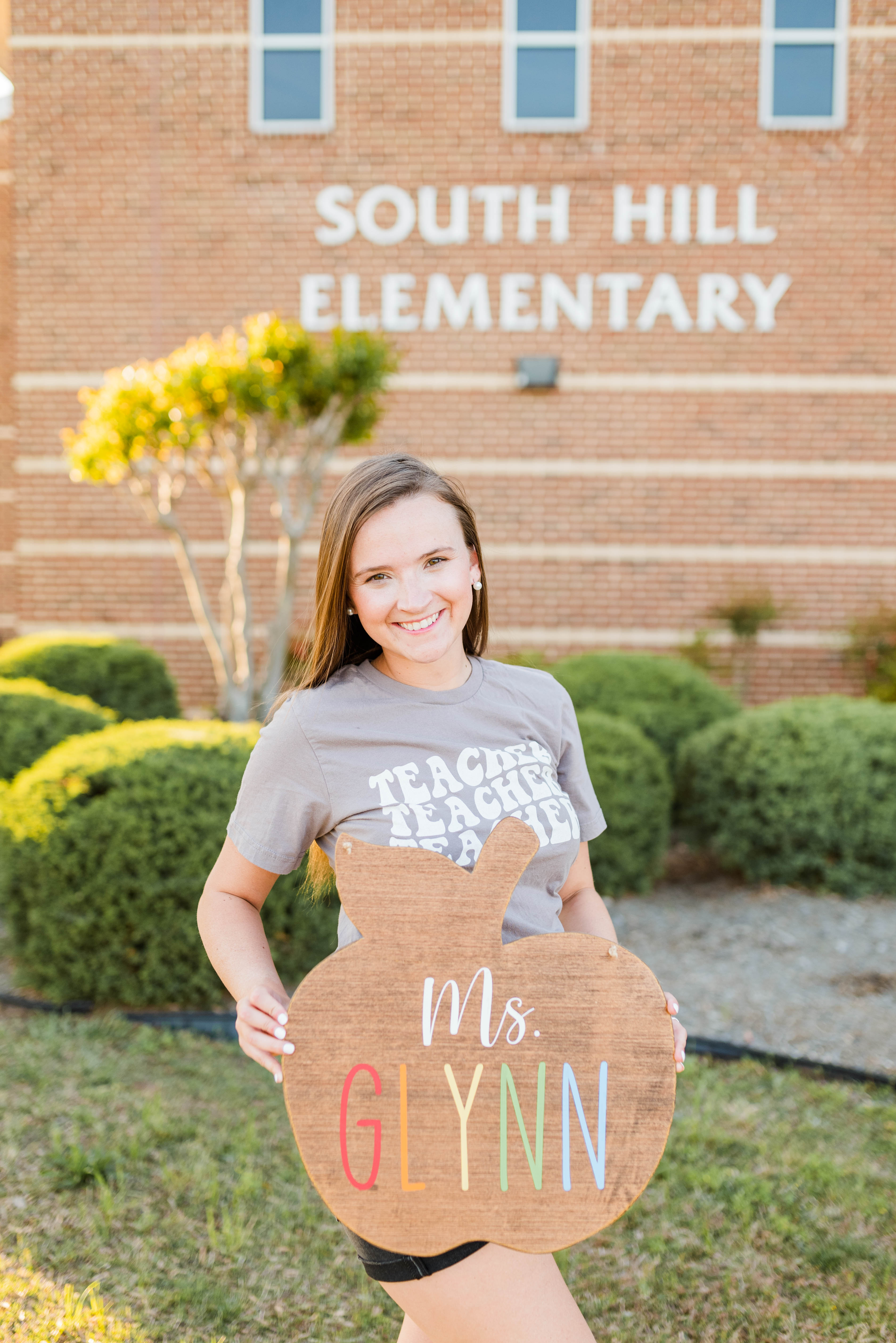 Glynn standing in front of school holding large apple sign with her name