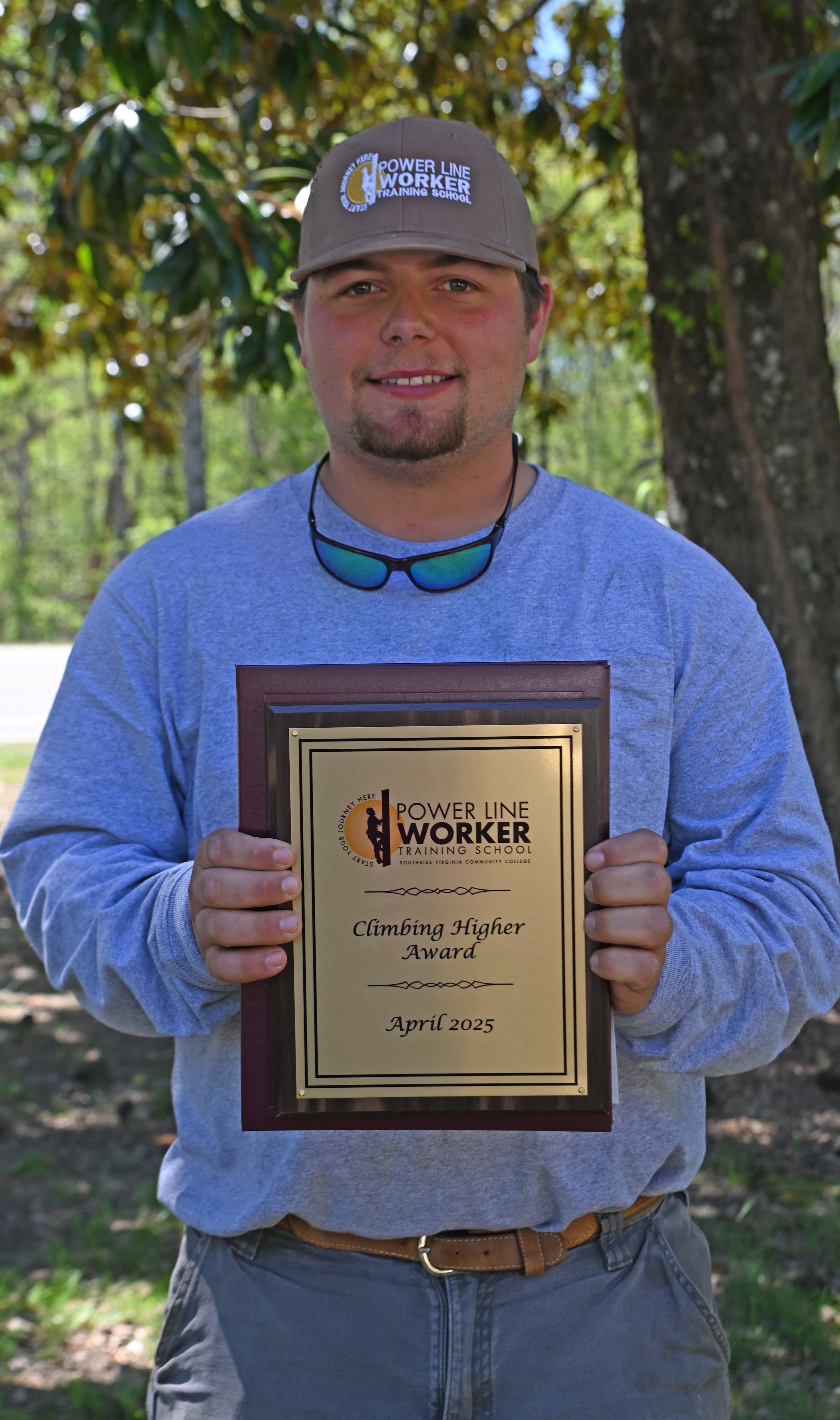 Kemp Davis of Tappahannock, holding the Climbing Higher Award standing beside a large tree