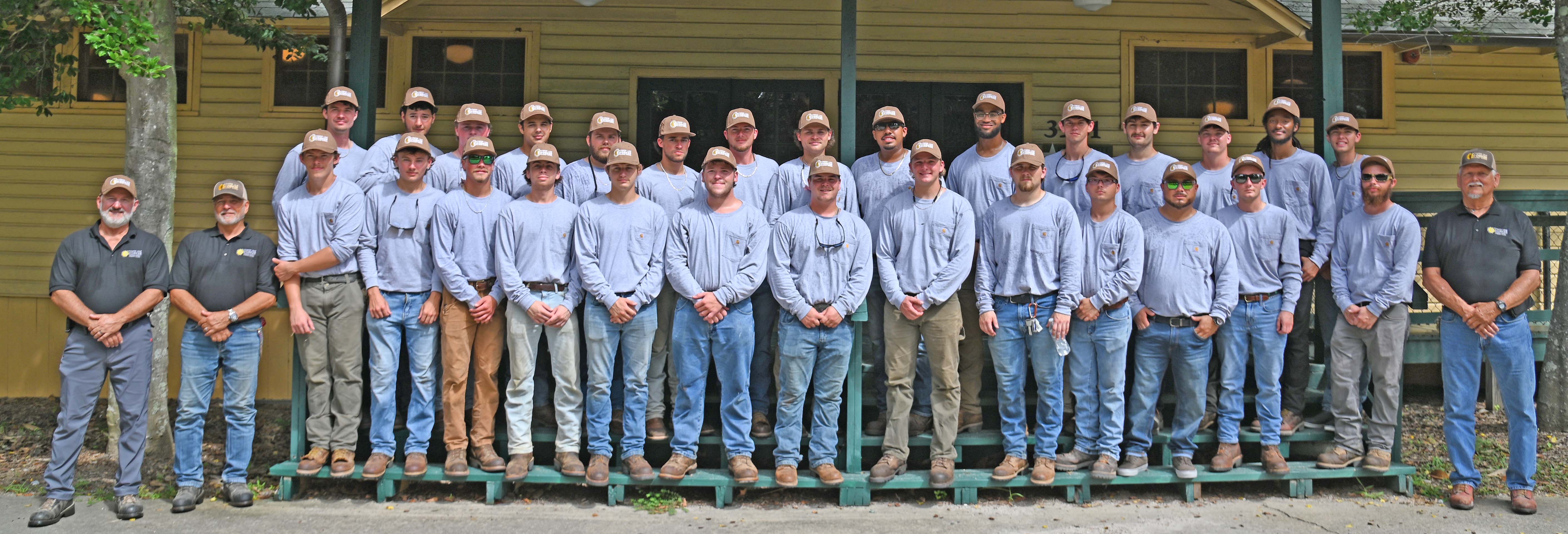 2 rows of Powerline graduates posed with instructors outside in front of a building
