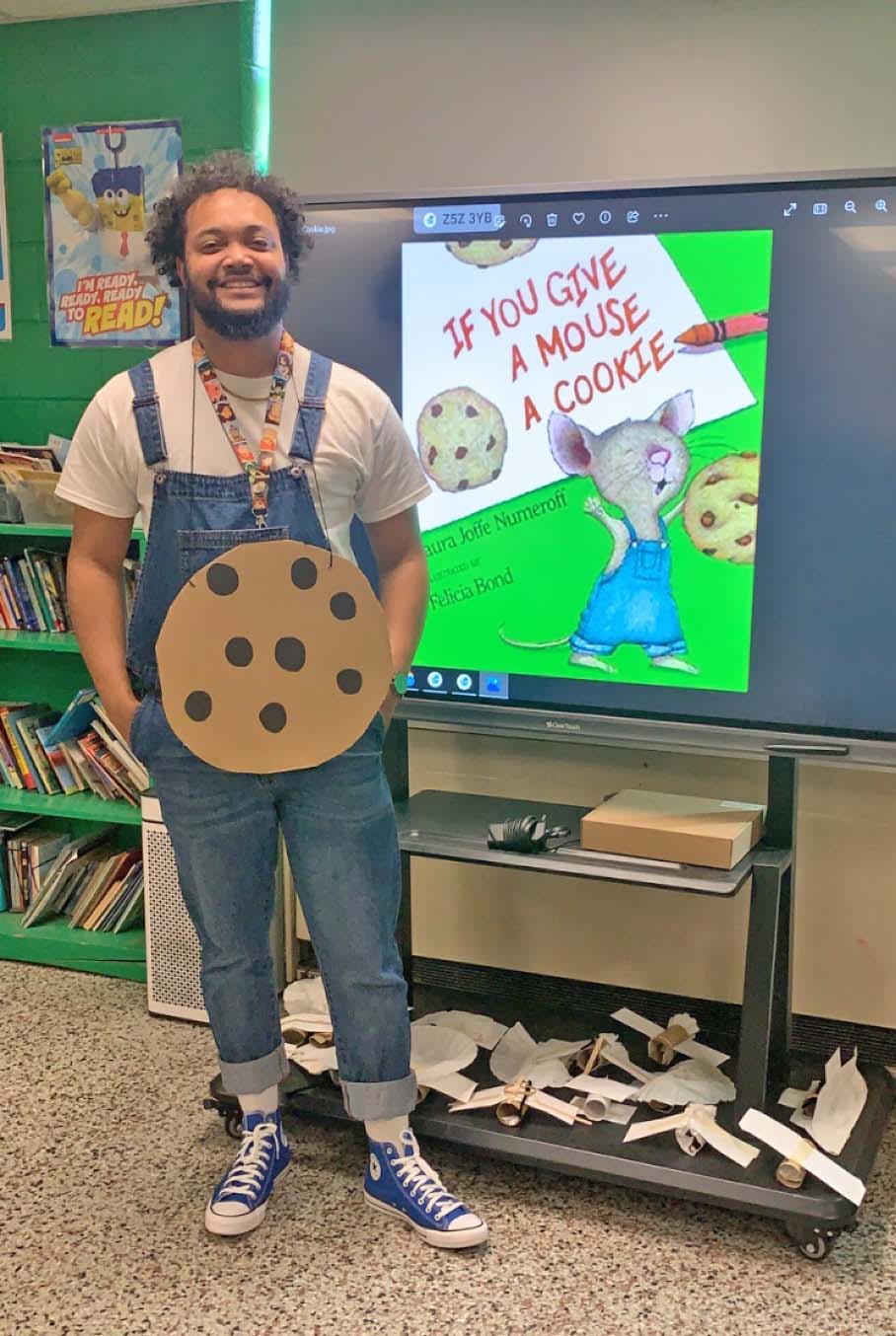 male teacher dressed as book character standing next to large screen displying book