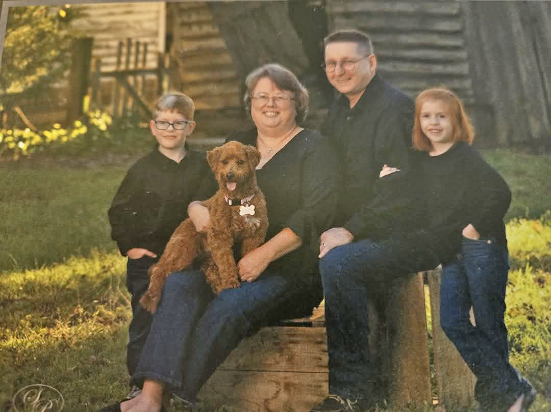Family of four posed with dog outside in front of tree and house