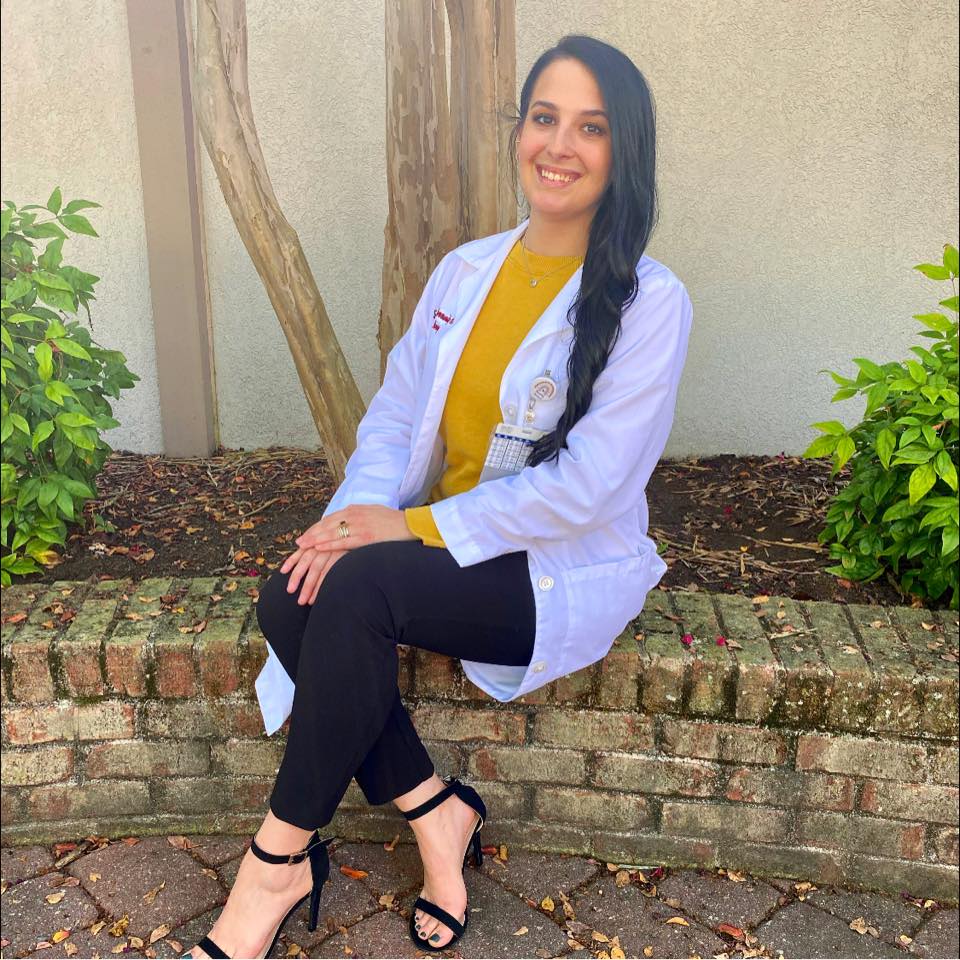 Nursing alumna Katrina Manning sitting on a low brick wall in front of a tree with her hands on her knees