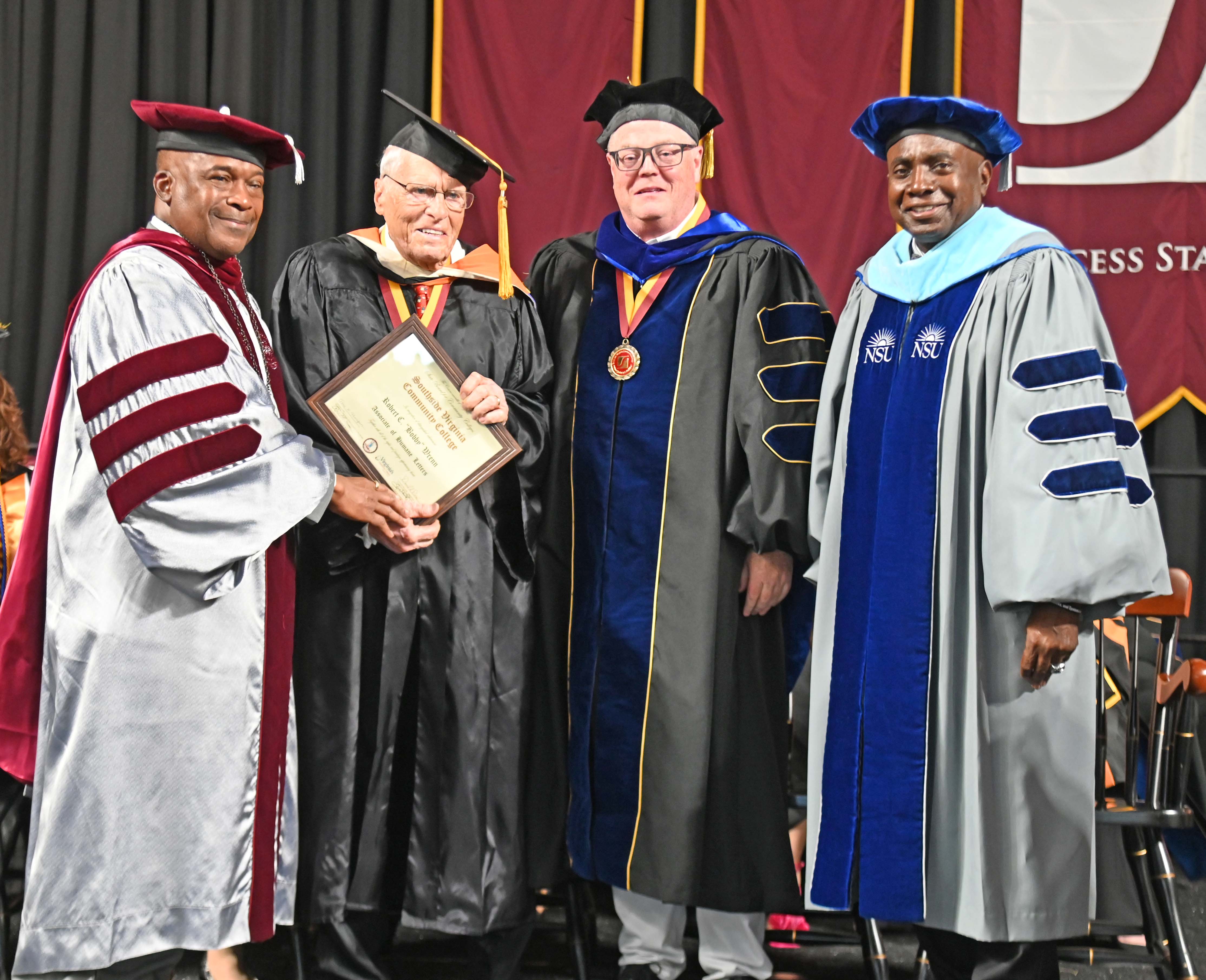 SVCC President Quentin Johnson handing honorary degree to Bobby Wren along side Vice President Keith Harkins and Local Board Chair Ronald Thornhill on stage in front of the SVCC banner