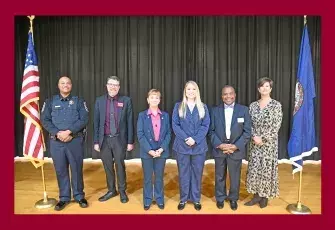 6 people standing on stage between 2 flags